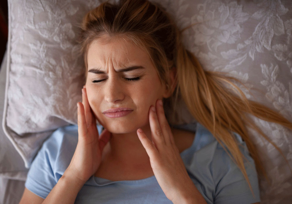 girl holding her jaw in discomfort while lying in bed
