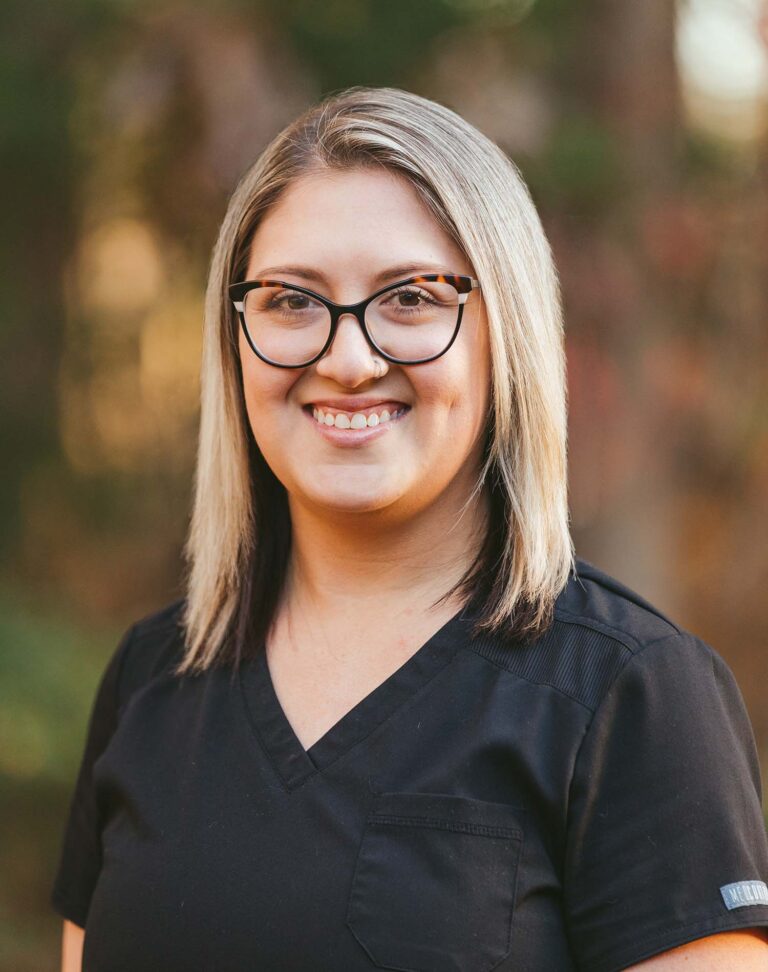 Headshot of Erin wearing a black jacket with Dinwiddie Dental logo on the right chest, the background is outdoors.