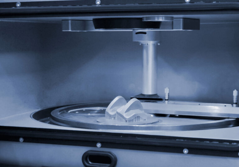 Close-up view of a 3D printer in operation, showcasing the creation of a complex object on a circular build platform with a vertical support structure above it.
